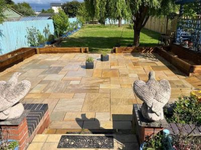 A patio with stone tiles features two bird statues at the entrance. The patio leads to a green lawn and a fenced backyard.