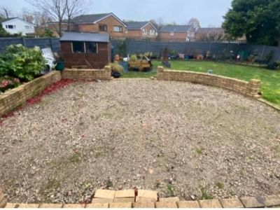 A gravel garden area is bordered by low brick walls and overlooks a lawn. A small shed and some plants are visible in the background.